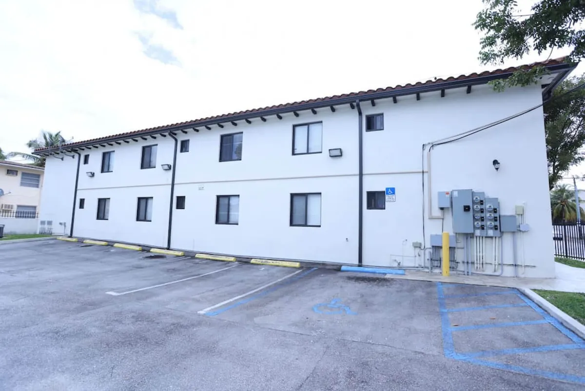 This exterior image shows the building's facade, several windows, and the adjacent parking lot. The practical and functional atmosphere highlights features like on-site parking and convenient access to the apartment entry. The visible parking spaces emphasize that guests can park right next to their door, while the secure and well-maintained exterior suggests peace of mind for longer stays.
